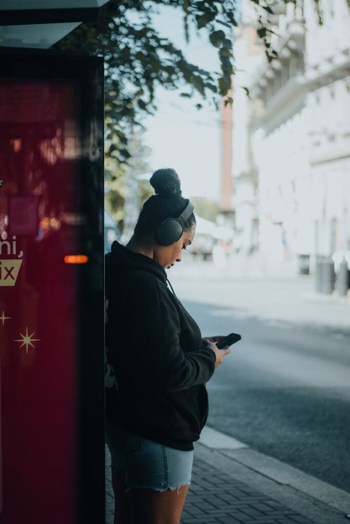 A woman is looking at her phone while standing on the side of the road