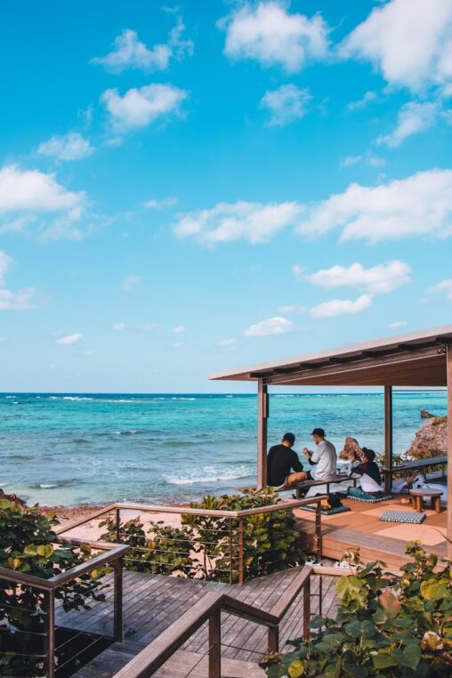 people sitting on brown wooden picnic table near sea during daytime